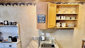 Une cuisine dotée d’un plan de travail en marbre, d’un évier, de meubles en bois et d’une pancarte indiquant : « Bienvenue au chalet ».