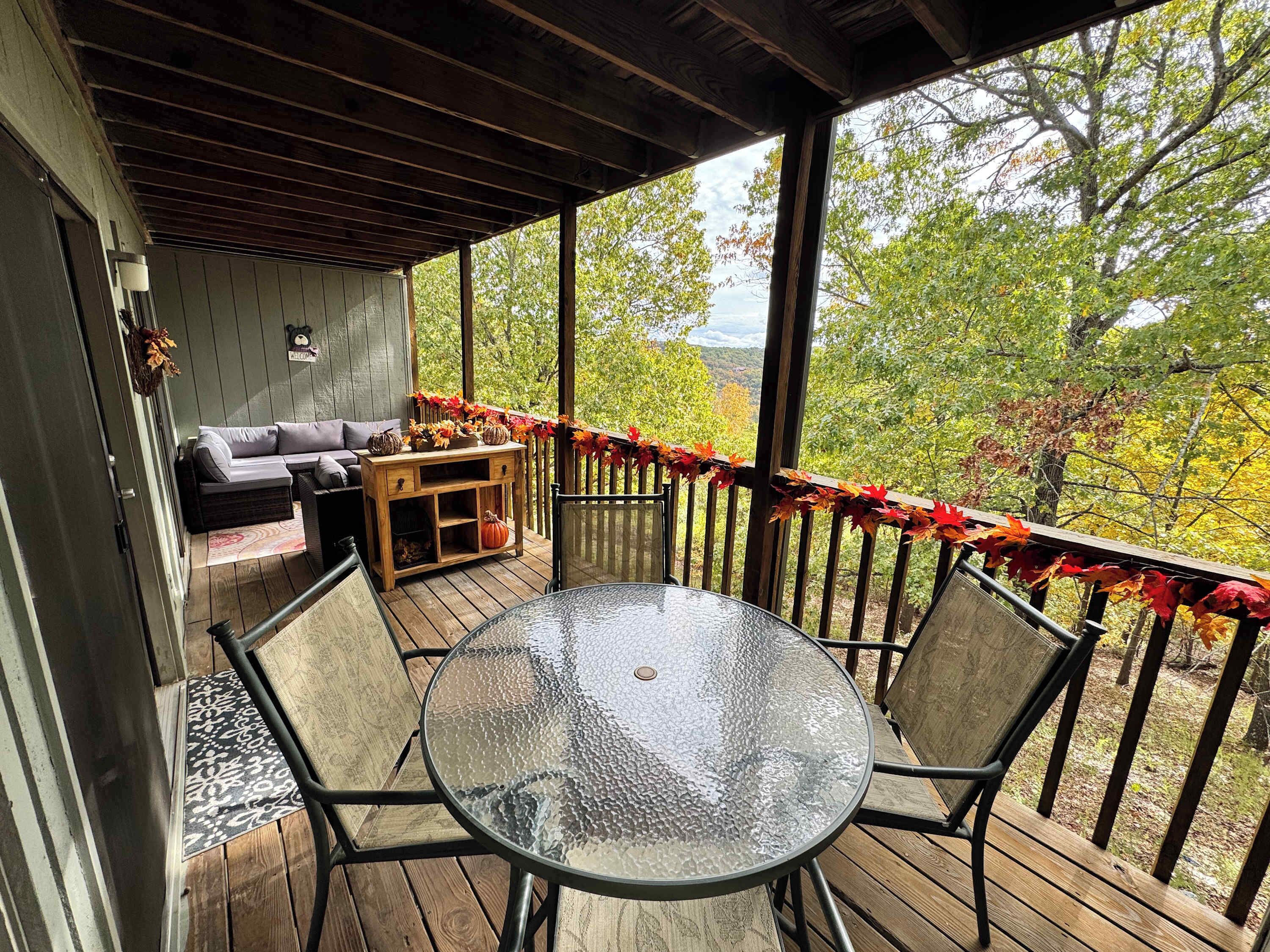 Un espace extérieur abrité, aménagé avec une table ronde en verre et des chaises, un canapé et un meuble en bois.