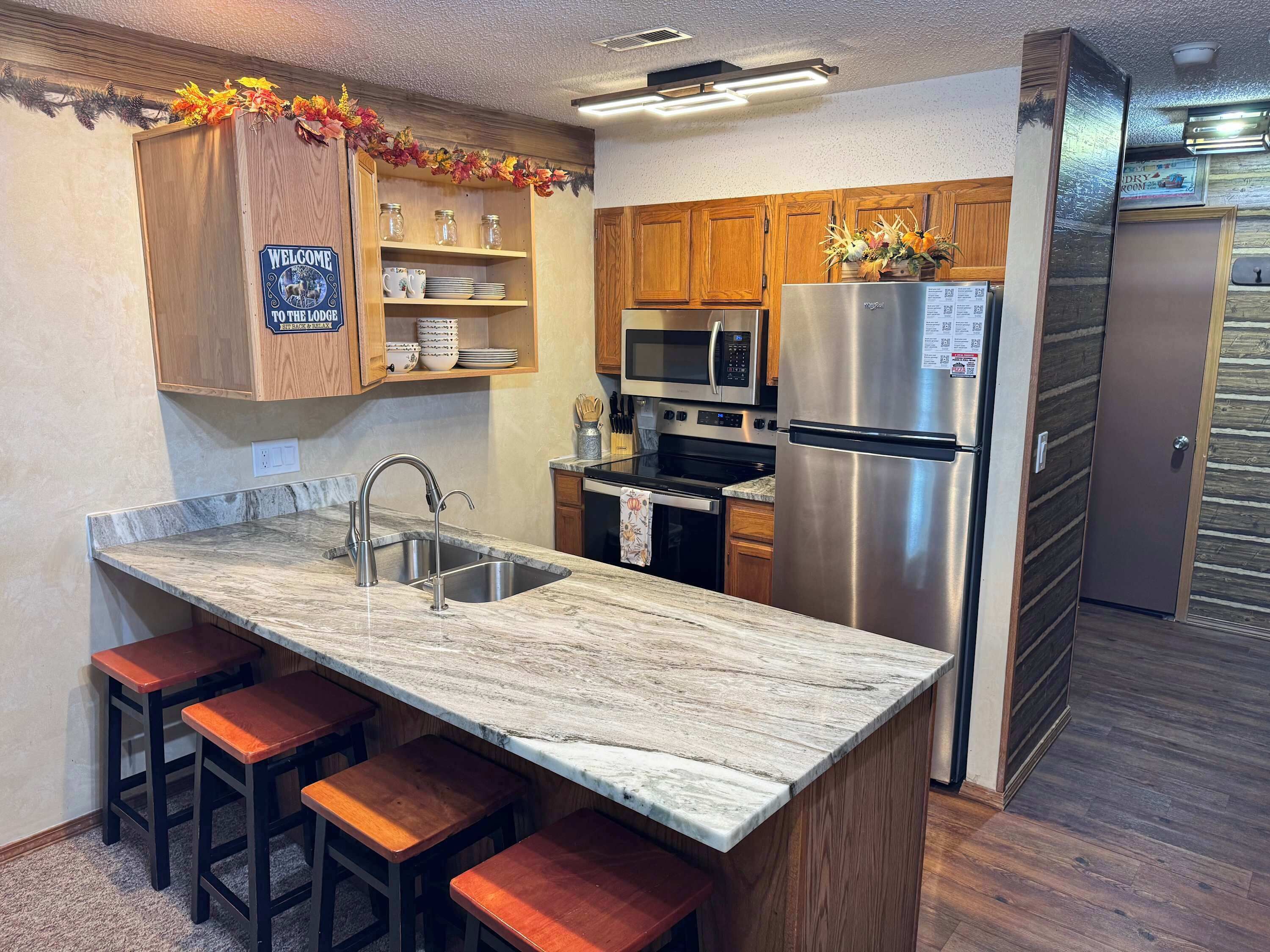 Una cucina con piano di lavoro in marmo, elettrodomestici in acciaio inossidabile, mobili in legno e un cartello con la scritta 'Welcome to the Lodge'.