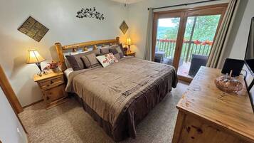 Une chambre dotée d’un grand lit, de deux tables de chevet avec des lampes, d’une tête de lit en bois, d’un ventilateur de plafond et d’une porte-fenêtre coulissante donnant sur un espace extérieur.