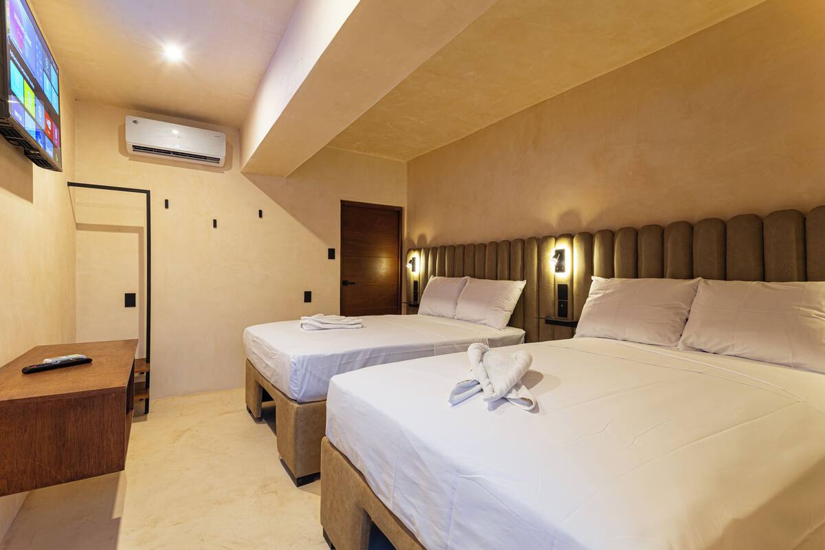 Una habitación de hotel con dos camas, televisión, aire acondicionado y una mesita de noche de madera.