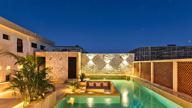 A swimming pool with a stone wall and a glass enclosure, surrounded by a building with a modern design. - Hotel Pakal 58 Centro (Mérida)