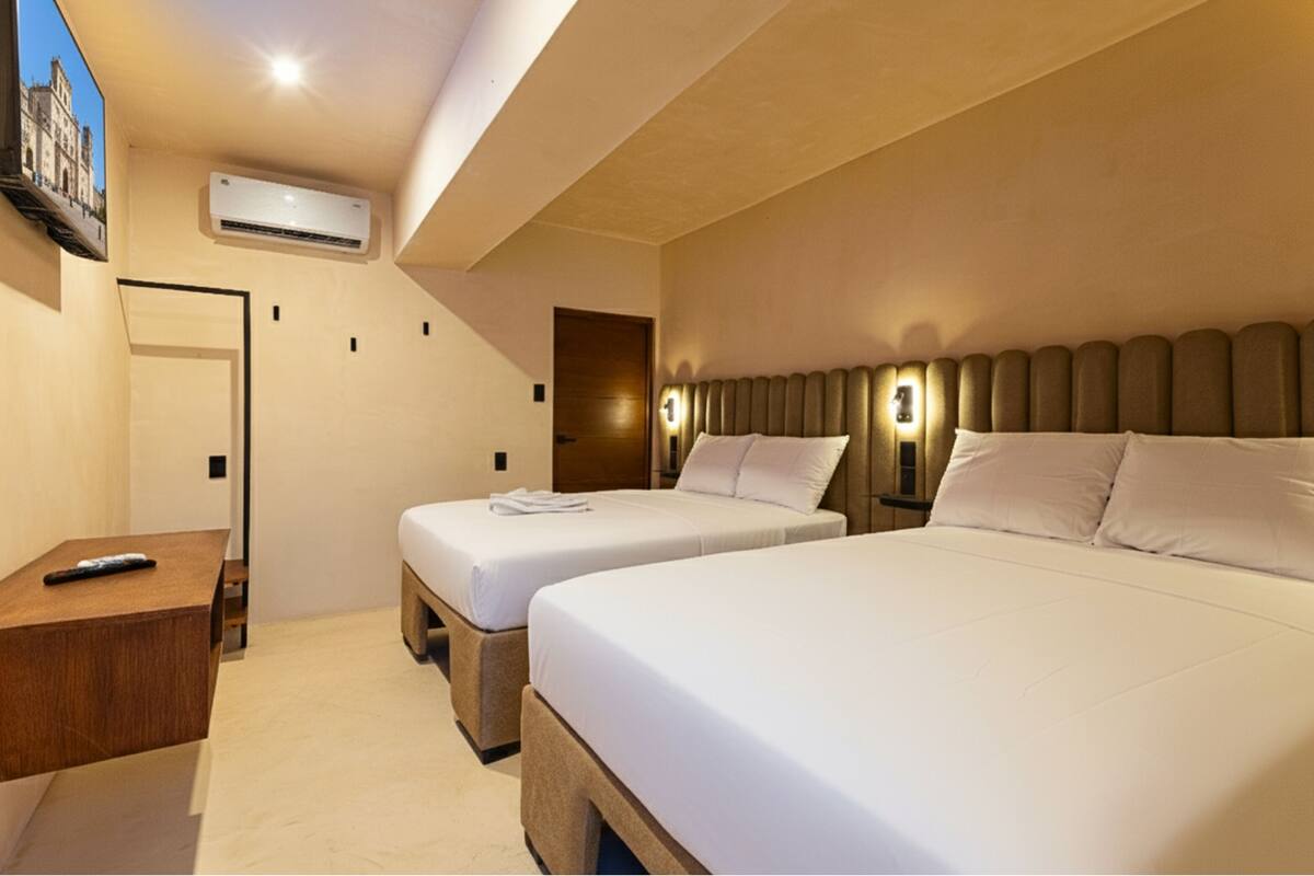 Habitación de hotel con dos camas, una mesita de noche de madera, un control remoto y un equipo de aire acondicionado en la pared.