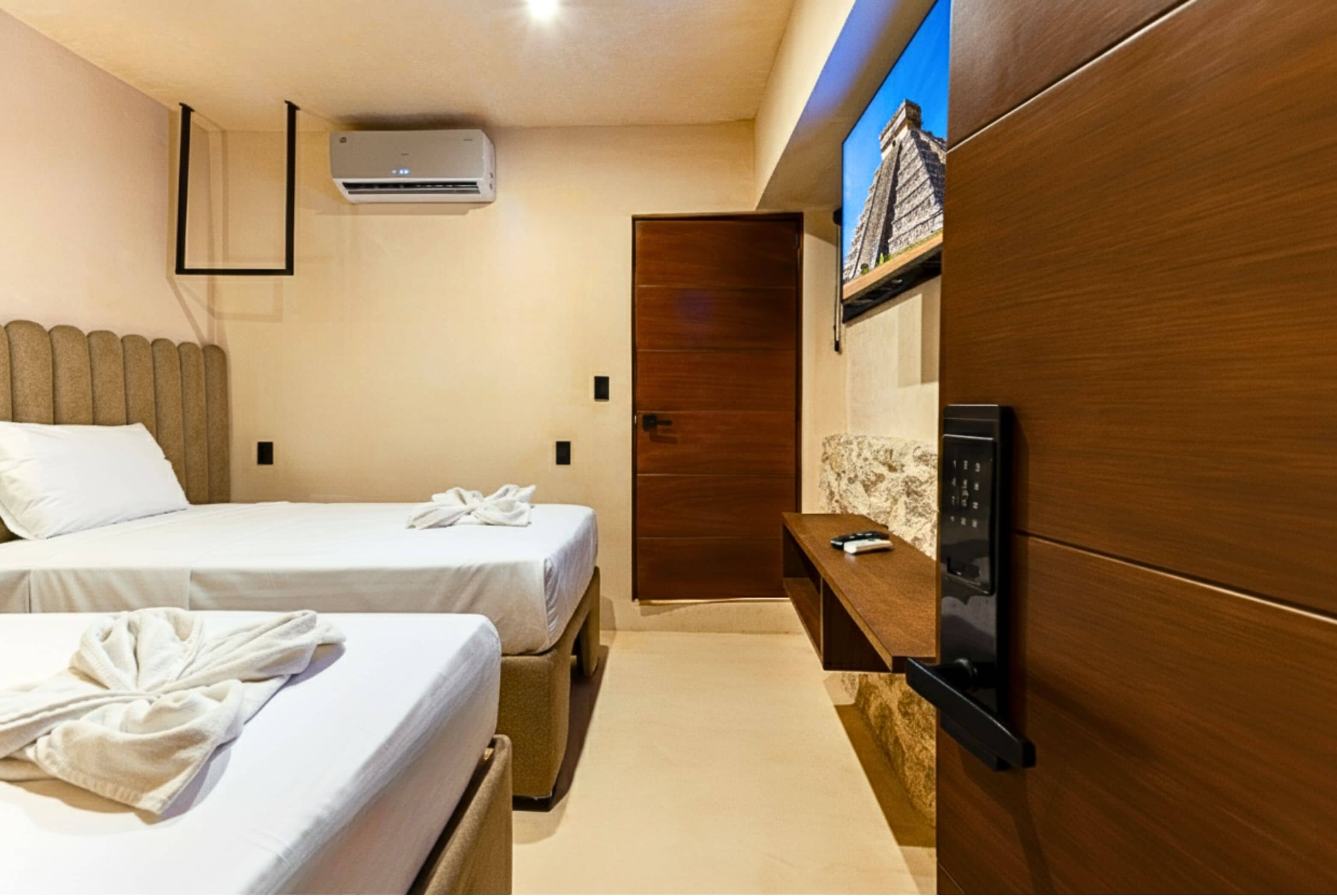 Habitación de hotel con dos camas, un armario de madera, televisor integrado y aire acondicionado.