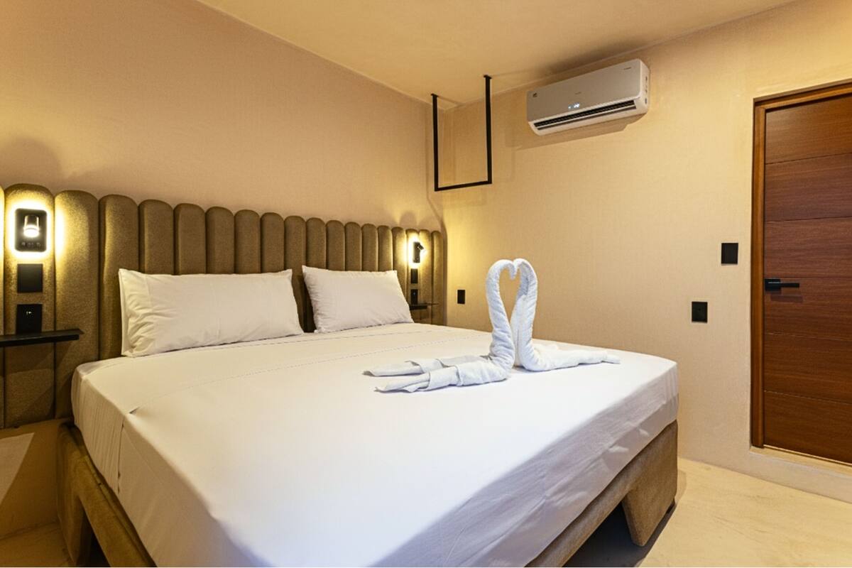 Una habitación de hotel con una cama bien hecha, un aire acondicionado de pared y una puerta de madera.