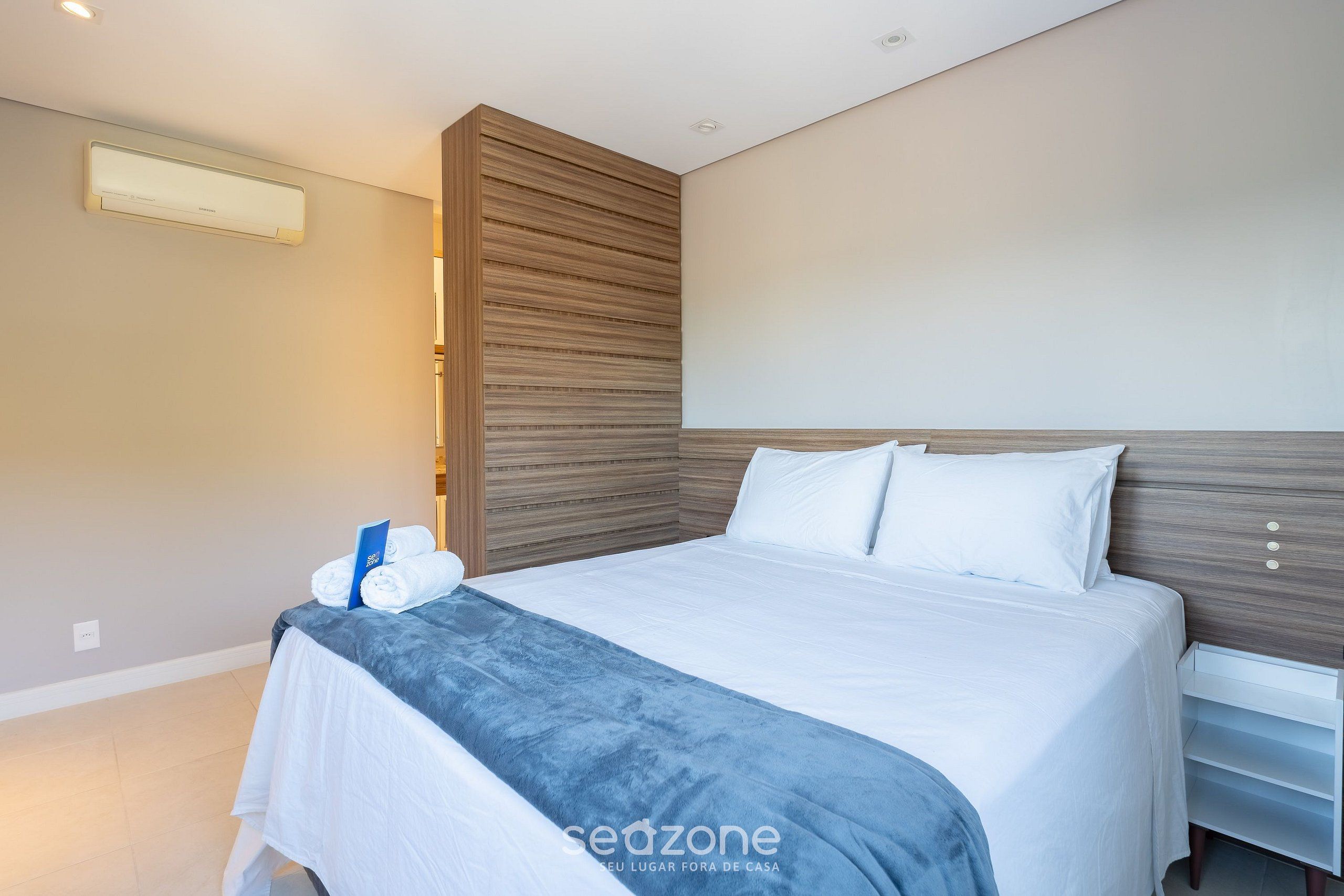 A modern hotel room with a large bed, a wooden headboard, and a bedside table.