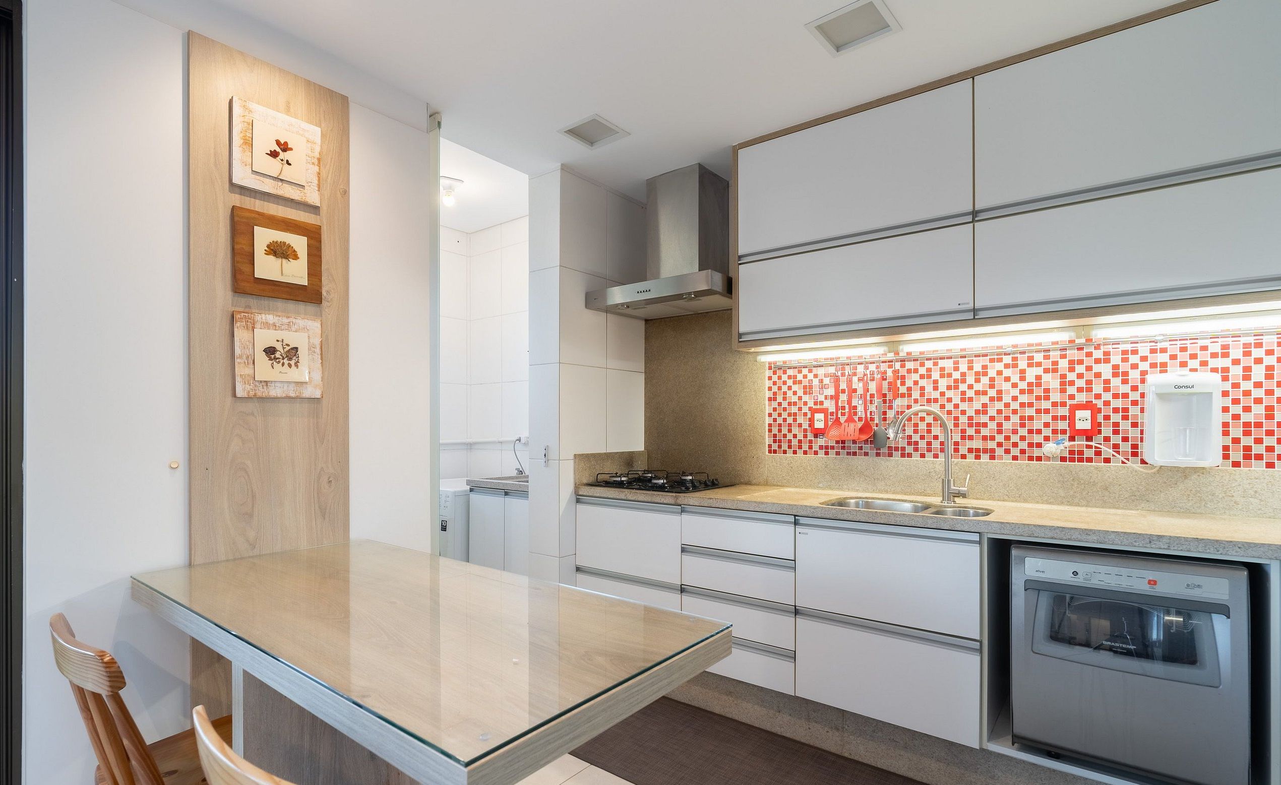 A modern kitchen with a glass-top dining table, white cabinetry, and a red and white backsplash.