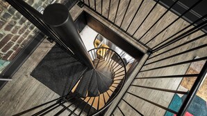 A spiral staircase with a black metal railing and a textured floor. - Stable #6 ~ Fire Pits, Mini Golf, Games, Walkable (Louisville)