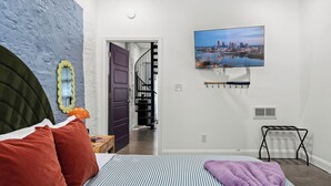 A bedroom with a bed, a view of a cityscape, a staircase, and a radiator. - Stable #6 ~ Fire Pits, Mini Golf, Games, Walkable (Louisville)
