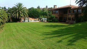 Un césped cuidado, una zona de piscina, un porche cubierto y una casa grande con múltiples ventanas y chimenea.