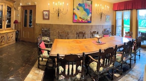 A large dining table with ornate chairs, a chandelier, and a colorful painting on the wall.