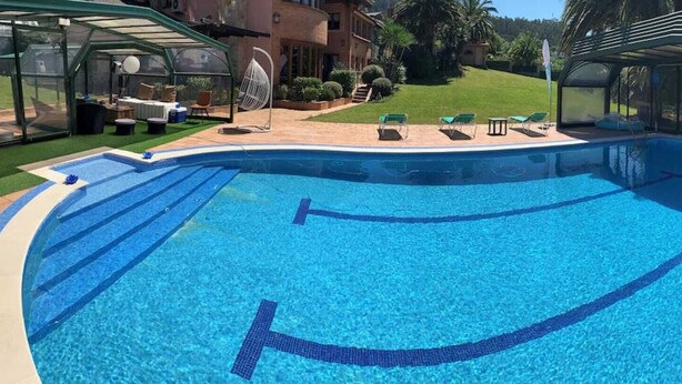 A swimming pool with a curved design, surrounded by lounge chairs and a covered seating area. - Yellow Room (Mungia)
