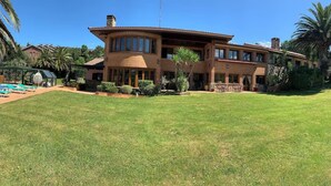 A two-story house with a large lawn, a pool, and palm trees. - Yellow Room (Mungia)
