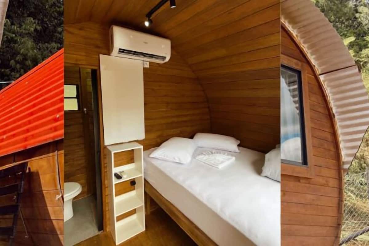 A wooden cabin with a single bed, a small bathroom, and a red roof.