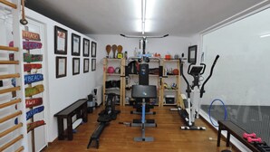 Un gimnasio en casa con equipo de ejercicio, una pared con diplomas enmarcados y un estante de madera con palas.