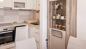 Une cuisine compacte équipée d’un four encastré, d’un lave-vaisselle et d’un petit plan de travail. On y trouve également un meuble avec une porte en verre, dans lequel sont rangés des services à thé et des bols.