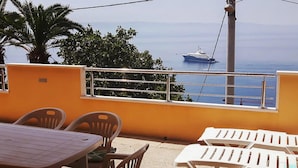 Une terrasse avec une table et des chaises, donnant sur une mer calme où se trouve un yacht.