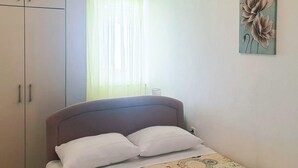 Une chambre à coucher comprenant un lit, une fenêtre avec des rideaux légers, une œuvre d’art accrochée au mur et une armoire.