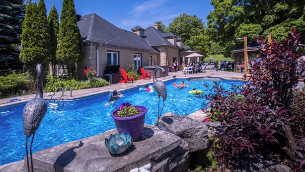 A swimming pool area with a house in the background, surrounded by greenery and a clear sky. - Forest Villa for Large Group with Outdoor Pool and indoor Swim Spa-Pet friendly (Newmarket)