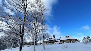 Een besneeuwd landschap met een groot huis, herkenbaar aan het symmetrische dak en de vele ramen.