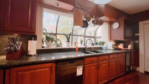 A kitchen with wooden cabinets, a window with plants, a sink, and a clock on the wall. - Forest Villa for Large Group with Outdoor Pool and indoor Swim Spa-Pet friendly (Newmarket)