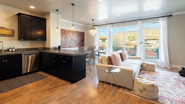 A modern kitchen with dark cabinetry, a dishwasher, and a dining area with a white sofa and a glass coffee table.
