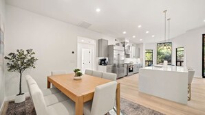 A modern kitchen with stainless steel appliances, a dining area with a wooden table and white chairs, and a large island with a sink. - Luxe Chapel home Heated pool/Spa, & Red Rock views (Sedona)