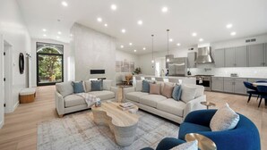 A modern living room with a large L-shaped sofa, a coffee table, and a blue armchair. There is a kitchen in the background with grey cabinets and stainless steel appliances. - Luxe Chapel home Heated pool/Spa, & Red Rock views (Sedona)