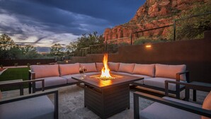 An outdoor seating area with a fire feature, cushioned sofas, and a view of a rocky landscape. - Luxe Chapel home Heated pool/Spa, & Red Rock views (Sedona)