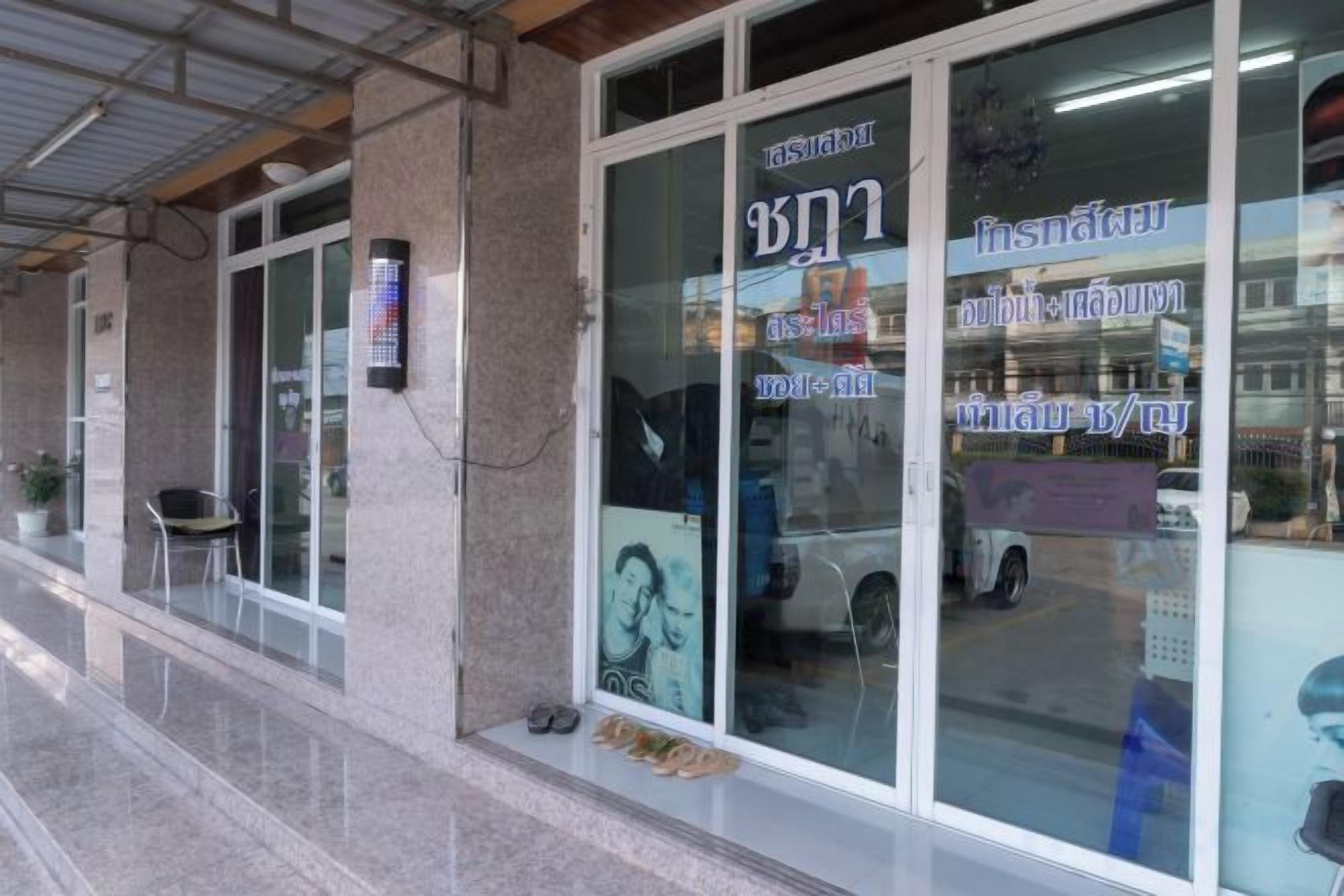 A building with large glass windows, a door with Thai text, and a small outdoor seating area.