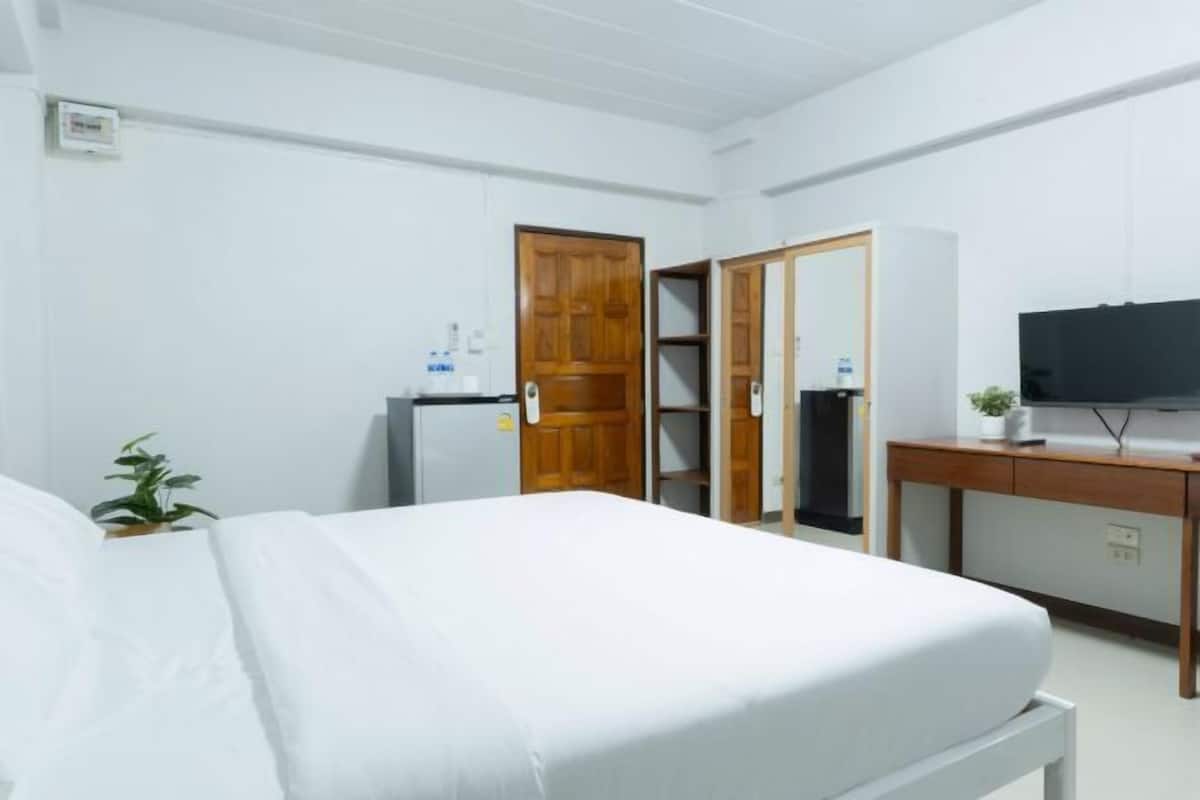 A hotel room with a bed, a desk with a television, a wardrobe, and a small plant.
