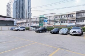 A parking lot with several cars, a building with a sign reading 'ATHENA,' and a tall building in the background. - Nicha Residense Hotel (Bangkok)