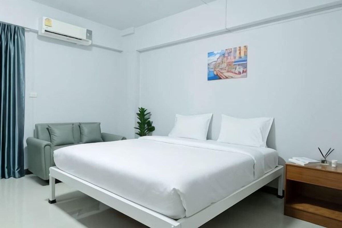 A modern hotel room with a bed, a bedside table, a chair, and a small plant.