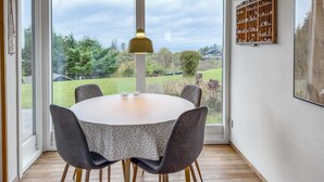 A dining area with a round table, four chairs, a pendant light, and a view of a garden through large windows. - Lovely home in Knebel with WiFi (Knebel)