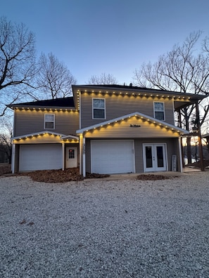 Une maison à deux étages avec un garage, une véranda et des guirlandes lumineuses.