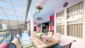 A covered outdoor patio with a table and chairs, a hanging flower pot, and a ceiling fan.