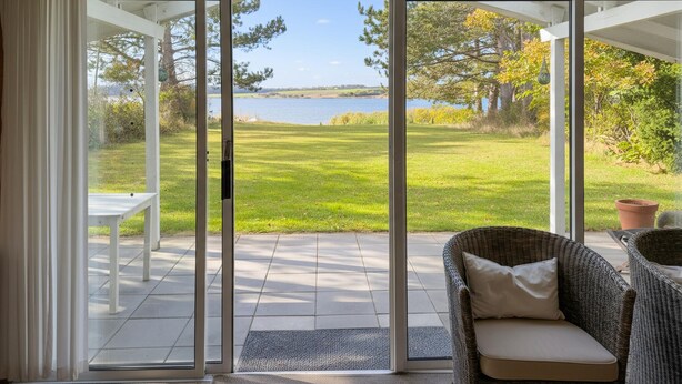 A covered patio with a sliding glass door leading to a grassy area with a view of a lake.