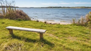 A bench by a lake with grassy banks and trees in the background.