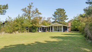A modern house with a covered patio, surrounded by a well-maintained lawn and trees.