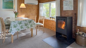 A cozy room with a wooden interior, a table with a floral tablecloth, a chair, a fireplace with logs, and a window with curtains.