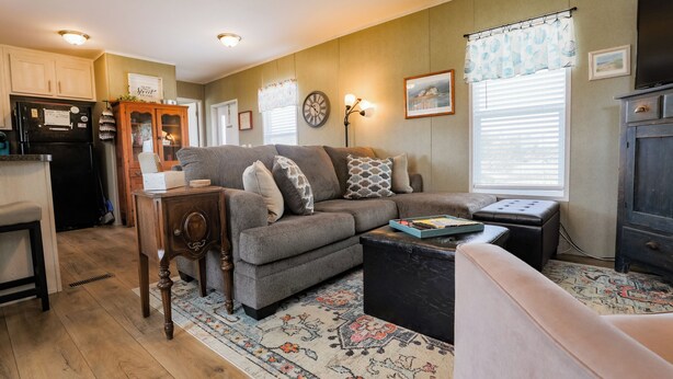 A cozy living room with a sofa, coffee table, and a rug. There is a kitchen area with cabinets and a refrigerator. - 3 BEDROOM, 2 BATHROOM, POND, SLEEPS 6 (Rockport)