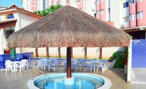 Un espace piscine agrémenté d’un parasol en chaume, de chaises longues et d’un panneau indiquant « HotSprings B3 Hotels ».