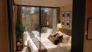 Une chambre avec un grand lit, un petit canapé, une plante en pot et une porte-fenêtre coulissante donnant sur un espace extérieur.