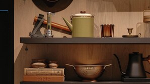 Une cuisine avec des étagères en bois où sont rangés divers ustensiles de cuisine, un chapeau suspendu et un climatiseur fixé au mur.