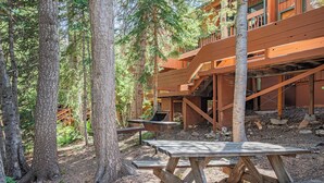A wooden cabin with a picnic table and a staircase leading to a deck.