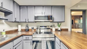 A modern kitchen with grey cabinets, stainless steel appliances, and a wooden countertop.