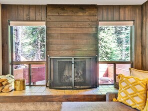 A corner fireplace with a screen, wooden walls, and large windows with a view of trees. - The Nest at Brian Head (Brian Head)