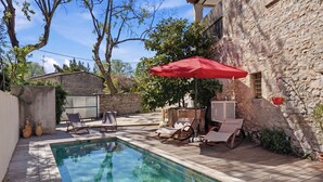 A swimming pool with wooden deck, lounge chairs, and a red umbrella. - Bardelours 1 – Charming house with swimming pool in the heart of the Pic Sa (Saint-Bauzille-de-Montmel)