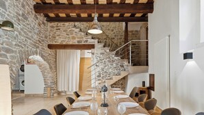 A dining area with a stone wall, wooden beams, a staircase, and a view of a laundry room. - Bardelours 1 – Charming house with swimming pool in the heart of the Pic Sa (Saint-Bauzille-de-Montmel)
