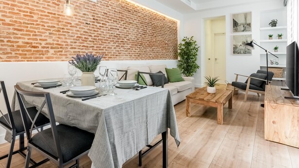 Un salon moderne avec un mur en briques, une table à manger dressée pour quatre personnes, un canapé, une table basse et un meuble pour la télévision.